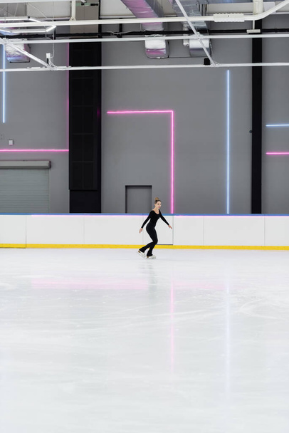 full length of figure skater in black bodysuit skating in professional ice arena - Photo, Image