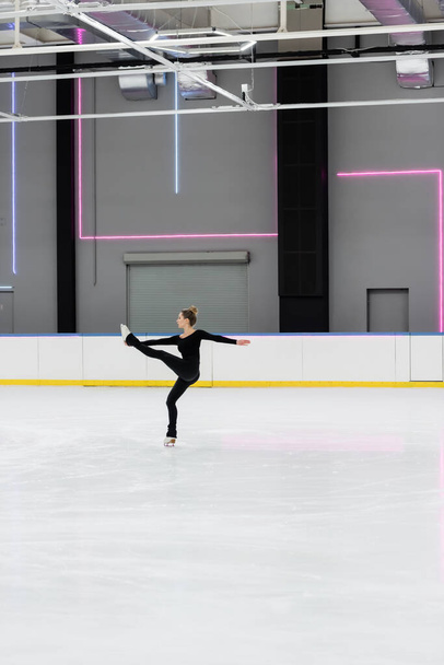 volledige lengte van kunstschaatser in zwart bodysuit oefenen in professionele ijs arena - Foto, afbeelding