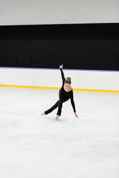teljes hossza fiatal szakmai műkorcsolyázó fekete karosszéria korcsolyázás kinyújtott kézzel jég arénában  - Fotó, kép