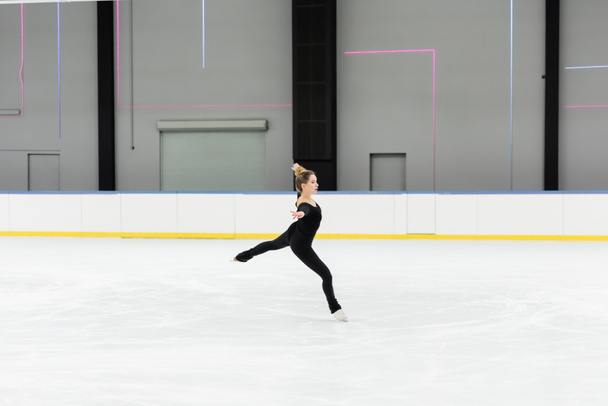 full length of professional figure skater in bodysuit skating with outstretched hands in ice arena  - Фото, изображение