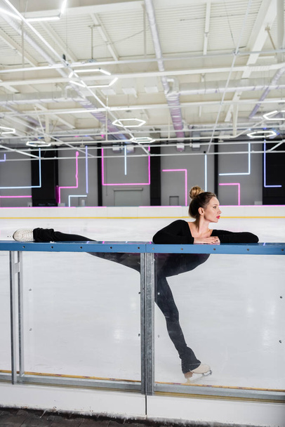 young woman in white figure skates stretching near ice rink  - Foto, Bild