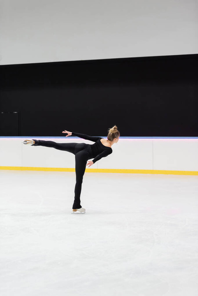 back view of professional figure skater in black bodysuit skating with outstretched hand in ice arena - Foto, afbeelding