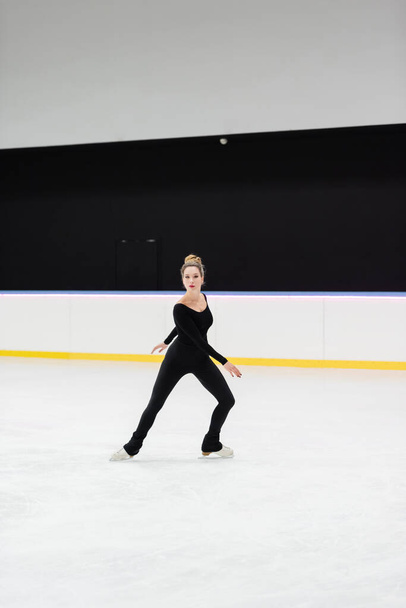 full length of professional figure skater in bodysuit skating in ice arena - Photo, Image