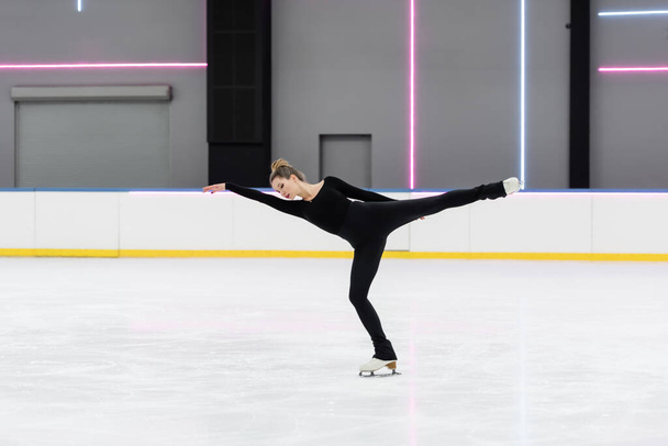 toute la longueur du jeune patineur artistique en body skating noir avec la main tendue dans l'arène de glace - Photo, image