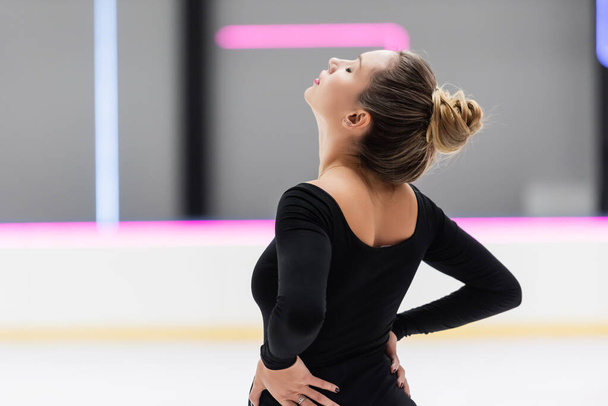 worried figure skater with closed eyes in black bodysuit stretching back - Foto, Bild
