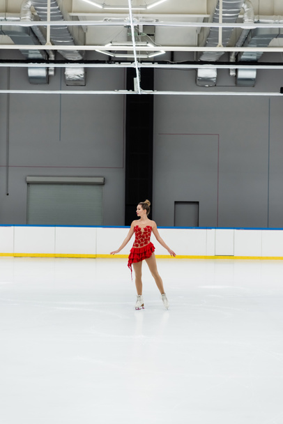 pełna długość młodego łyżwiarza figurowego w sukience wykonującego taniec na profesjonalnej arenie lodowej - Zdjęcie, obraz