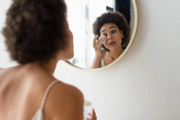 Mujer afroamericana borrosa limpiando la cara con almohadilla de algodón en el baño  - Foto, imagen