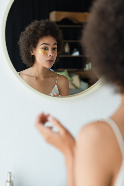 Femme afro-américaine floue avec bandeau oculaire regardant miroir à la maison  - Photo, image