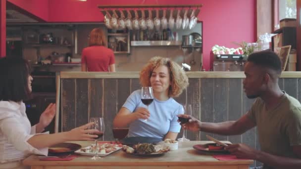 Gruppo di amici che fanno un brindisi con il vino in un ristorante - I giovani seduti a un tavolo tostare godere il pasto - Filmati, video