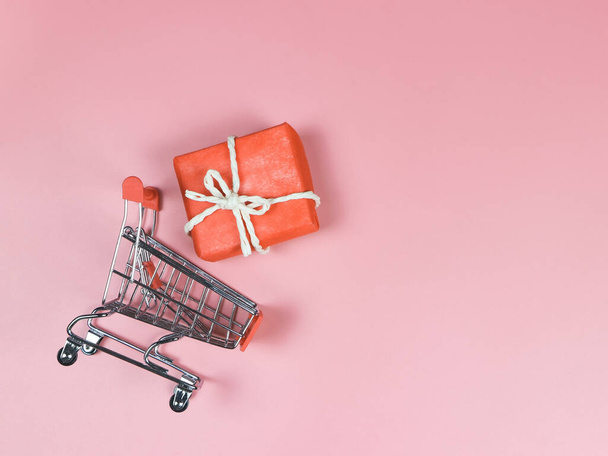 Top view or flat lay of shopping trolley with red gift box on pink background.  holiday shopping concept. - Photo, Image
