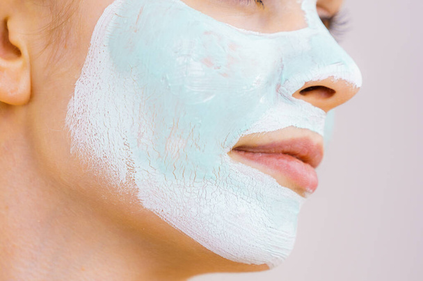 Young woman with white green mud mask on her face. Teen girl taking care of oily skin, cleaning the pores. Beauty treatment. Skincare. - Φωτογραφία, εικόνα