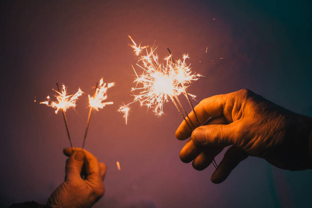 hands of elderly couple holding sparkles celebrating New Year - Photo, Image