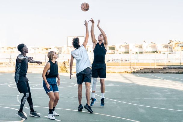 Skupina přátel skákání jako hrát basketbal ve venkovním kurtu - Fotografie, Obrázek