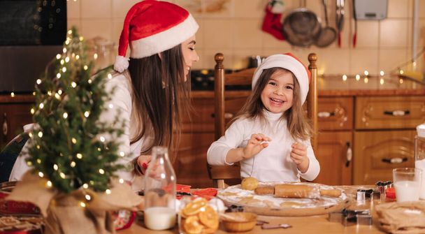 Process of mom and daughter baking at home. Raw dough for cooking Christmas cookies gingerbread on wooden table. Candle light at evening time. Fir tree - Фото, зображення