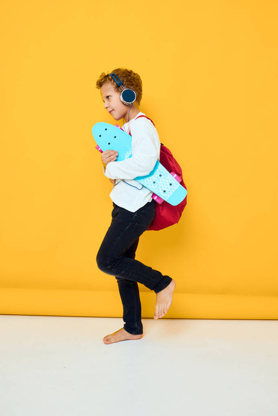 joyful boy with a red backpack wearing skateboard headphones isolated background - Photo, image