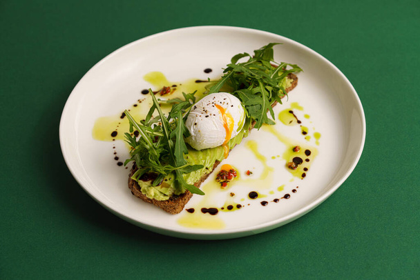 Tost awokado z gotowanym jajkiem na zielonym tle, poziomo - Zdjęcie, obraz