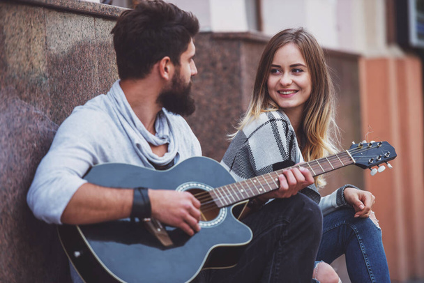 Портрет молодой счастливой пары, играющей на гитаре, стоя на лестнице в городе
 - Фото, изображение