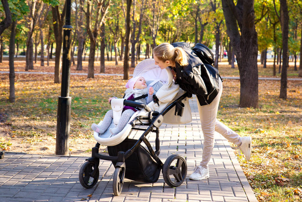 Glückliche Mutter geht mit ihrem Kind im Park spazieren. Mutter neben dem Baby im Kinderwagen. Spaziergang an der frischen Luft. - Foto, Bild