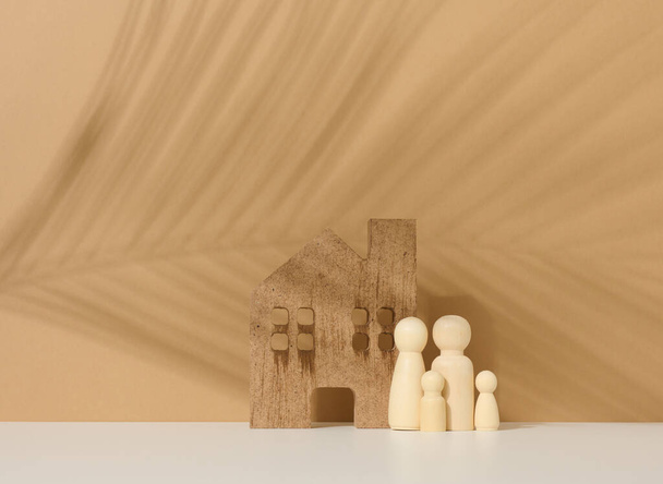 dřevěné rodinné figurky, modelový dům na hnědém pozadí. Nákup nemovitostí, koncepce pronájmu. Stěhování do nových bytů - Fotografie, Obrázek