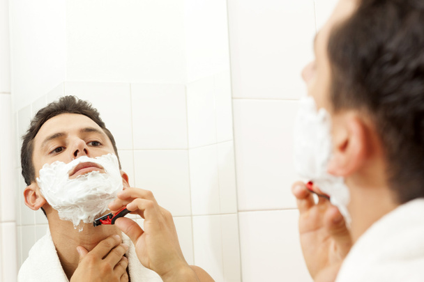 Young man shaving his beard with razor at the bathroom - 写真・画像