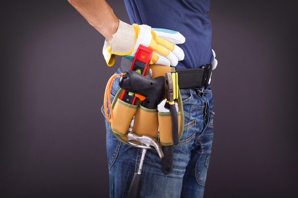 Close-up de um trabalhador com cinto de ferramentas e capacete contra costas pretas
 - Foto, Imagem