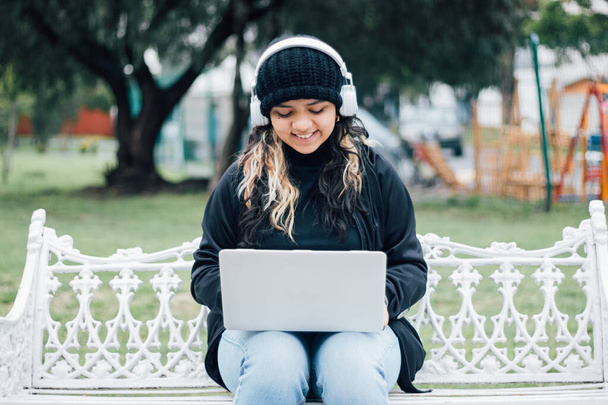 Latina adolescente menina da faculdade sentado em um banco no parque usando um laptop - Foto, Imagem
