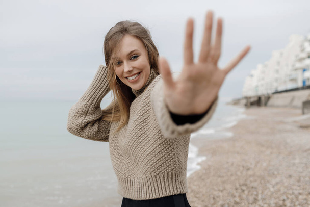 portrait of a young smiling woman in cozy wear outdoor hand in camera give me five - Fotó, kép