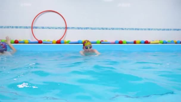 Kleines Kind in Schutzbrille, Mütze Praxis im Pool mit blauem Wasser, Züge. Kleiner Junge schwimmt zur Seite, dreht sich um und schwimmt zurück. Konzept der aktiven Freizeit. Innenansicht. Zeitlupe. - Filmmaterial, Video