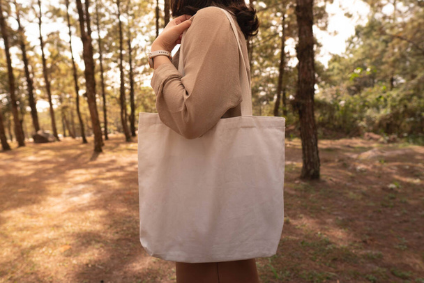 Blank white tote bag canvas fabric with handle mock up design. Close up of woman holding eco or reusable shopping bag at park. No plastic bag and ecology concept. - Foto, Imagem