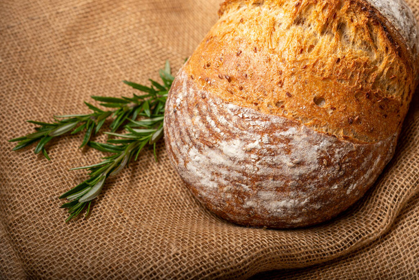 Sourdough bread with Italian herbs and rosemary isolated on burlap cloth. - Фото, зображення
