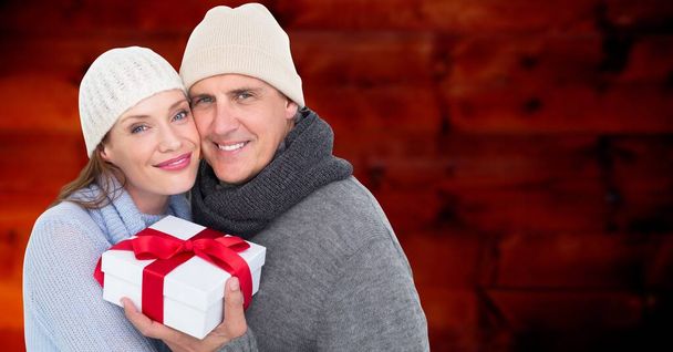 Composite image of caucasian senior couple holding a gift box against red textured background. christmas festivity and celebration concept - Foto, immagini