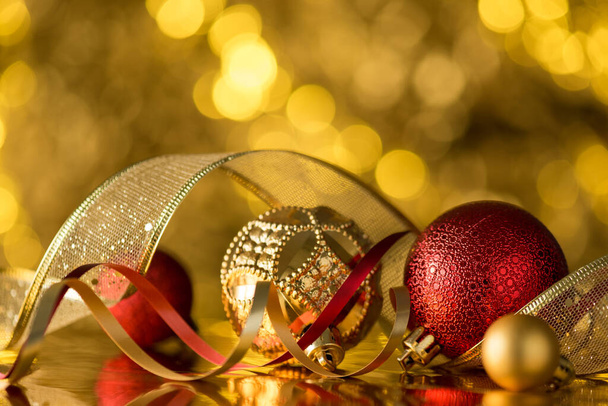 Foto de primer plano de oro y rojo decoraciones del árbol de navidad adornos bolas serpentina y cinta sobre fondo bokeh dorado - Foto, imagen