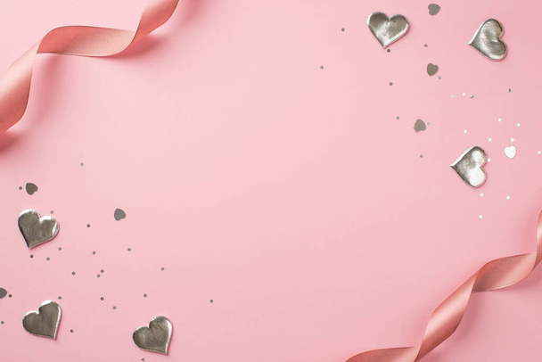 Top view photo of st valentine's day decorations curly silk ribbon silver hearts sequins and heart shaped confetti on isolated pastel pink background with copyspace in the middle - Foto, imagen
