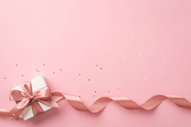 Sevgililer Günü dekorasyonunun en üst görüntüsü. Beyaz hediye kutusu. Pembe kıvrımlı kurdele ve izole edilmiş pastel arka plan üzerinde pullar. - Fotoğraf, Görsel