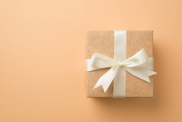 Top view photo of saint valentine's day decorations craft paper giftbox with white ribbon bow on isolated beige background with copyspace - 写真・画像