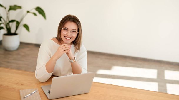 Smiling young woman working online on netbook at wooden table - Foto, imagen