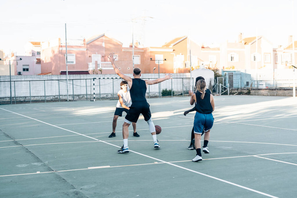 Four friends playing basketball together in an outdoors court - 写真・画像