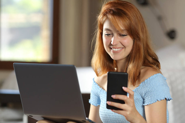 Happy woman using laptop and mobile phone in a house room - Foto, Bild