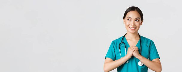 Sağlık çalışanları, virüsü önleme, karantina kampanyası konsepti. Kararlı ve kendinden emin, önlüklü Asyalı kadın doktor ellerini kenetleyip, hazırlanıyor, sol üst köşeye bakıyor. - Fotoğraf, Görsel
