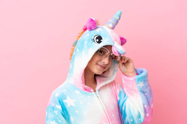 Little caucasian girl wearing a unicorn pajama isolated on pink background - Photo, image