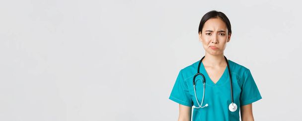 Zdravotničtí pracovníci, prevence viru, koncepce karanténní kampaně. Detailní záběr skeptické a zdráhavé ženské asijské lékaře, zdravotnický pracovník v křoví vypadající nespokojeně, bílé pozadí - Fotografie, Obrázek