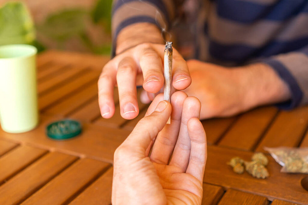Personas sentadas en una mesa durante una fiesta compartiendo un porro de cannabis. - Foto, imagen