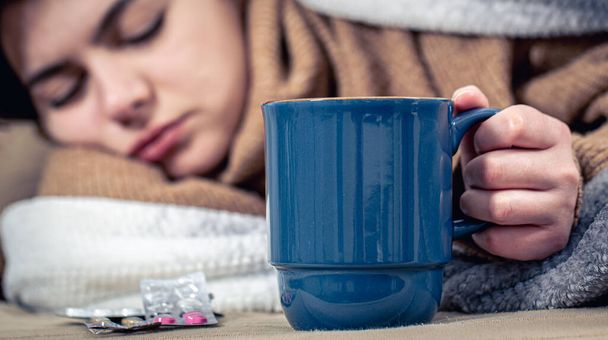 若い女性は飲み物のカップとベッドに横たわっています,ホームトリートメント,寒さ. - 写真・画像