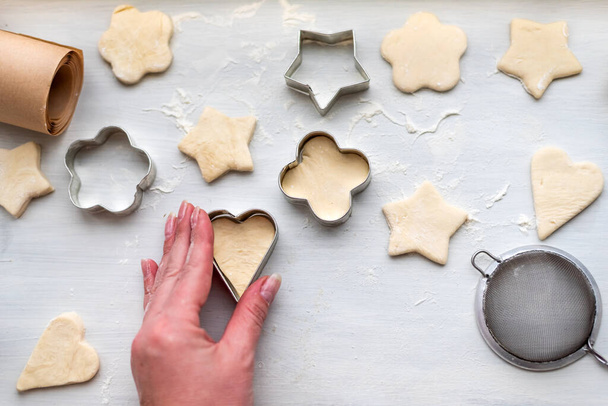 Top view of woman hands cooking a gingerbread cookie in the form of heart, star, cloud and flower. Christmas and New Year concept, festive preparations for winter hilodays - Foto, Bild
