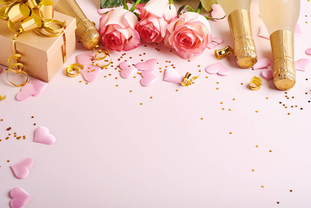 Pink roses flowers, champagne, gift, golden ribbons and confetti red hearts on pink background. Top view flat lay with space for your greetings. Valentines day background and greeting card. - Fotografie, Obrázek