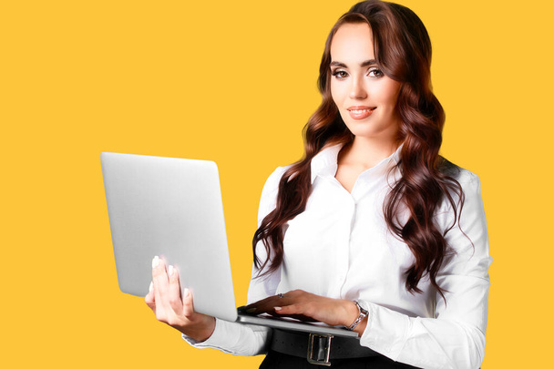 Ceci est portrait de belle fille caucasienne de 30 ans avec ordinateur portable dans ses mains sur fond jaune. - Photo, image