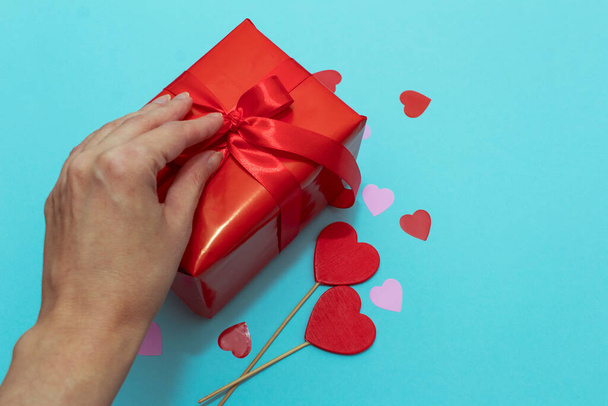 Rote Schachtel mit roter Schleife auf blauem Papierhintergrund. Valentinstagsgeschenk mit Konfetti und Dekor - Foto, Bild