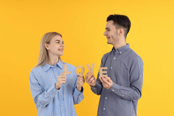 Linda pareja sostiene palabra amor sobre fondo amarillo - Foto, Imagen