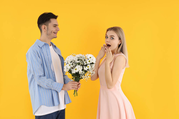 Un ragazzo dà un bouquet a una ragazza su sfondo giallo - Foto, immagini
