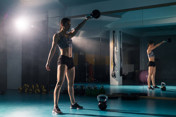 A fit young woman doing exercise with a kettlebell weight in the gym. - 写真・画像